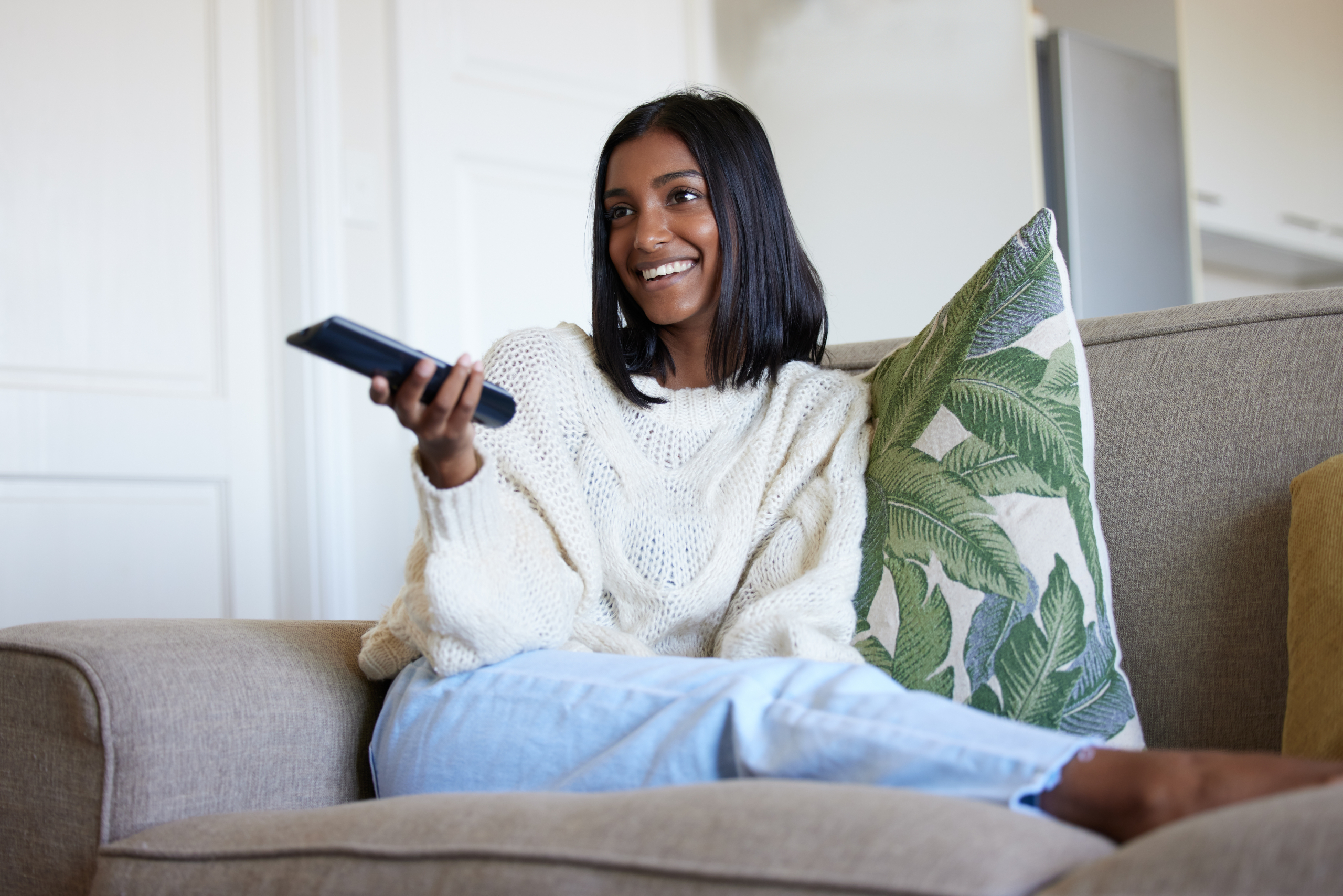 Shot of a beautiful young woman holding a remote control while sitting on the couch at home.