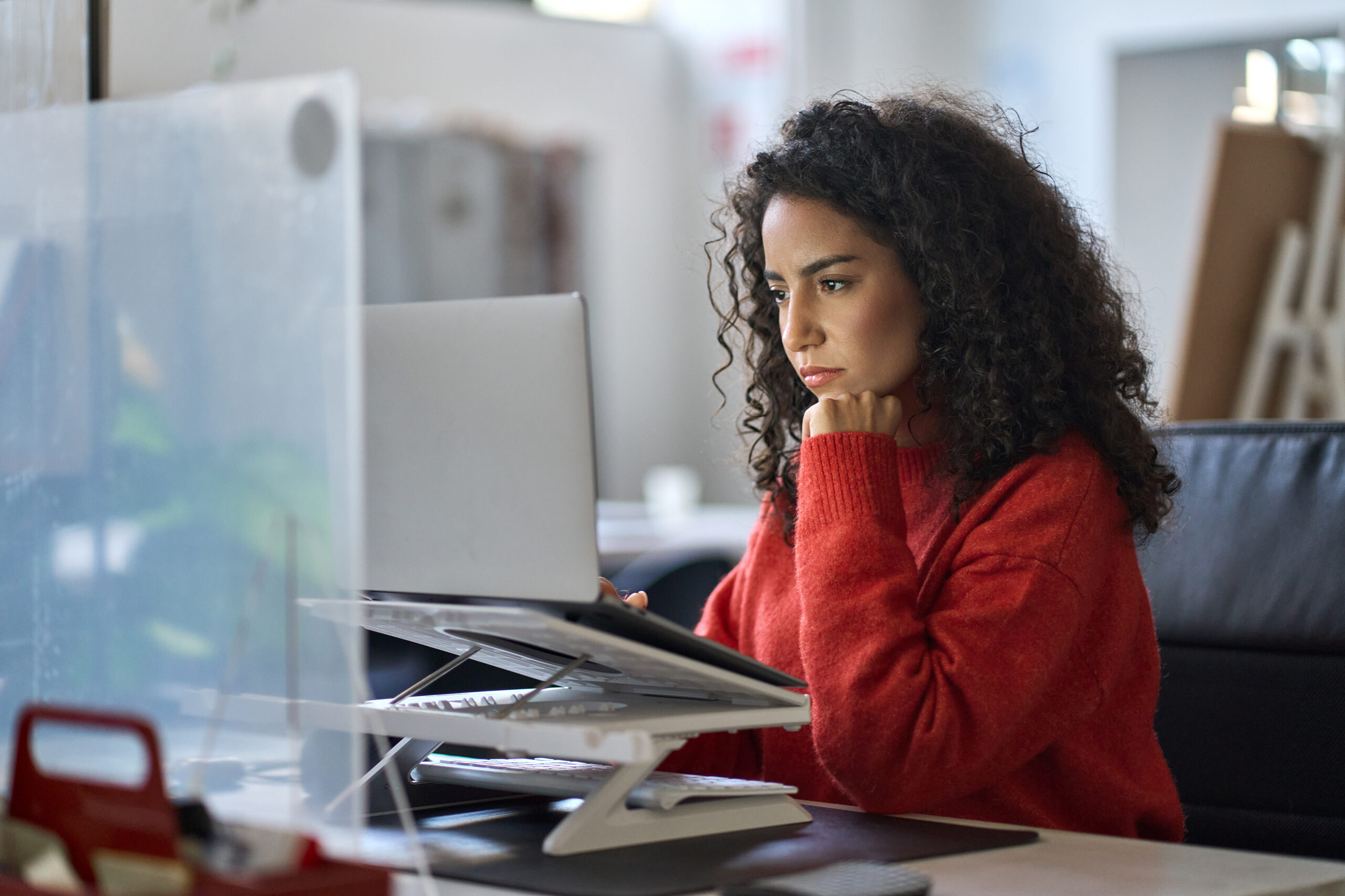 Young latin professional business woman office worker analyst sitting at desk working on laptop thinking on project plan, analyzing marketing or financial data online, watching elearning webinar.